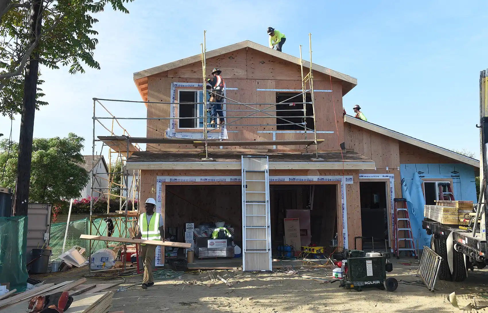 A home under construction with three men in hardhats working on different areas of the home.