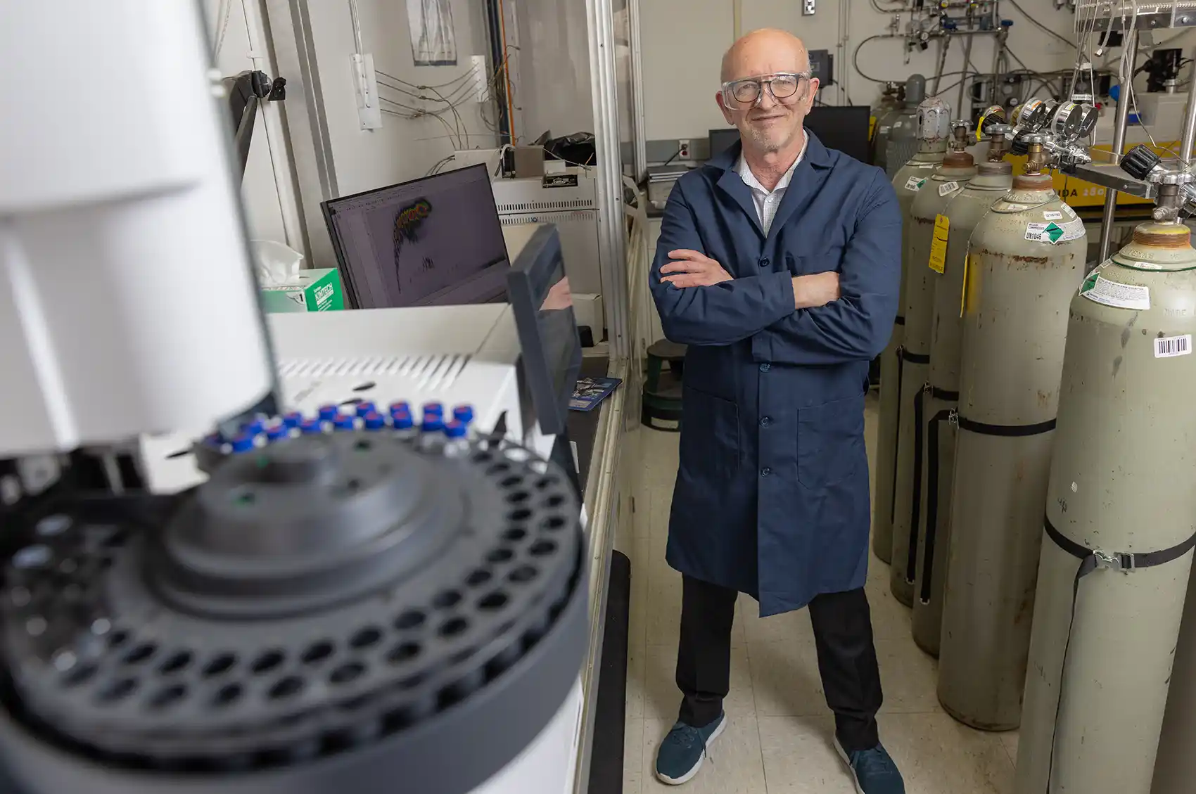 A person stands with their arms crossed next to a 2D gas chromatograph coupled to a time-of-flight mass spectrometer