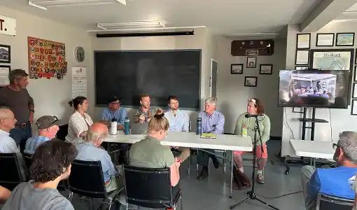 Continue reading about People sit in a room and face a table where six people are seated.