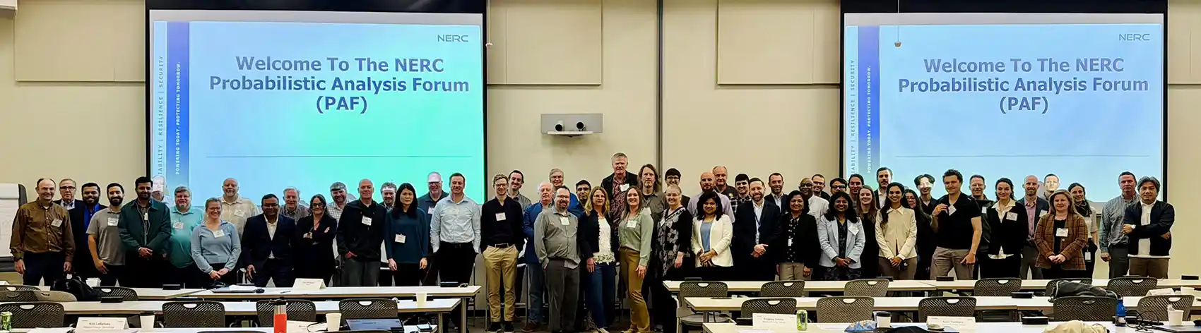 A large group of people posing in front of two screens with the text Welcome to the NREC Probabilistic Analysis Forum (PAF)