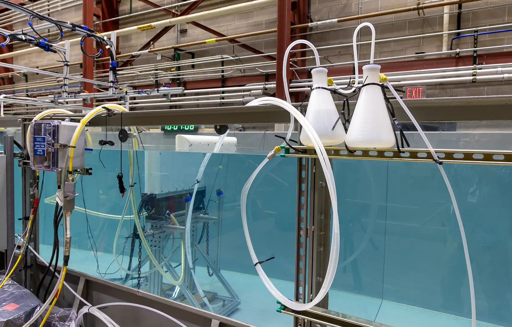 Side view through the glass wall of a wave tank in a laboratory showing the underwater testing apparatus inside the tank.