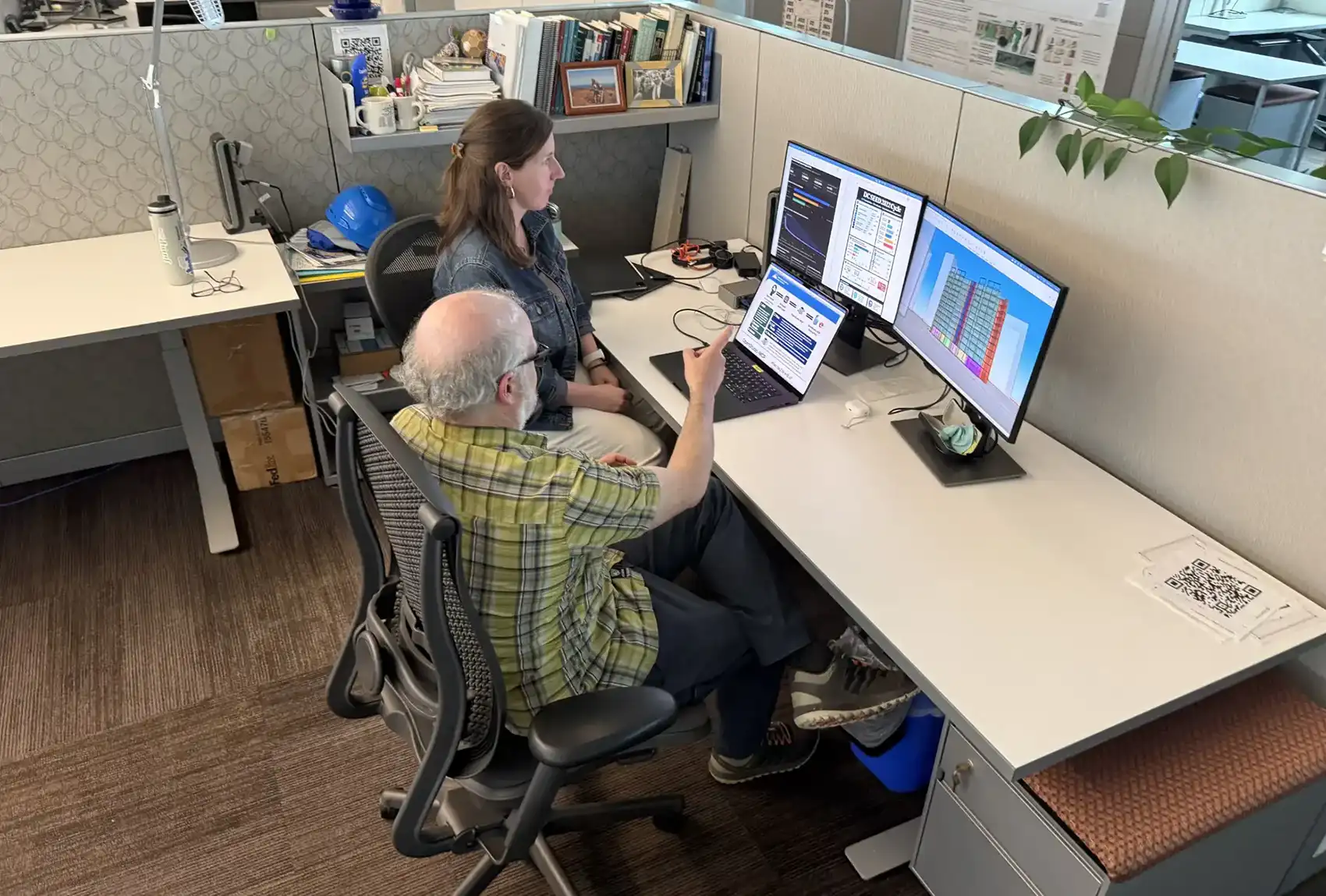 20260916-no-more-speaking-in-code-building-energy-modeling-made-easy-mcp Two people sit at a desk with three computer screens.