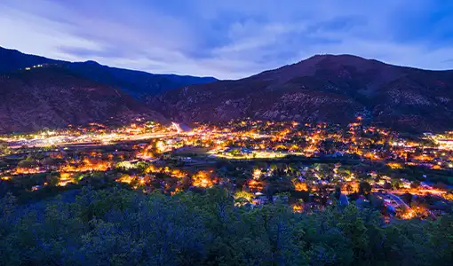 Overlooking town lit up at twilight with mountains in background.
