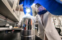 One researcher with safety glasses and a face mask working on equipment in a lab.