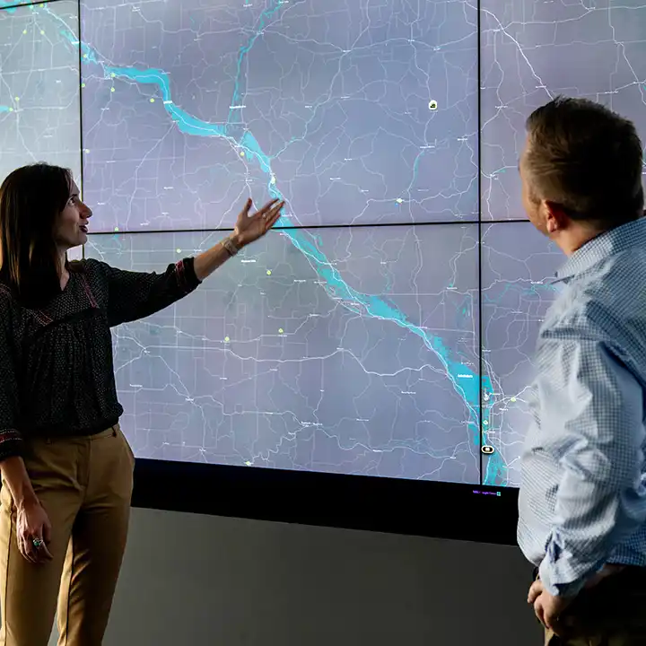 Two people look at grid data on large screen