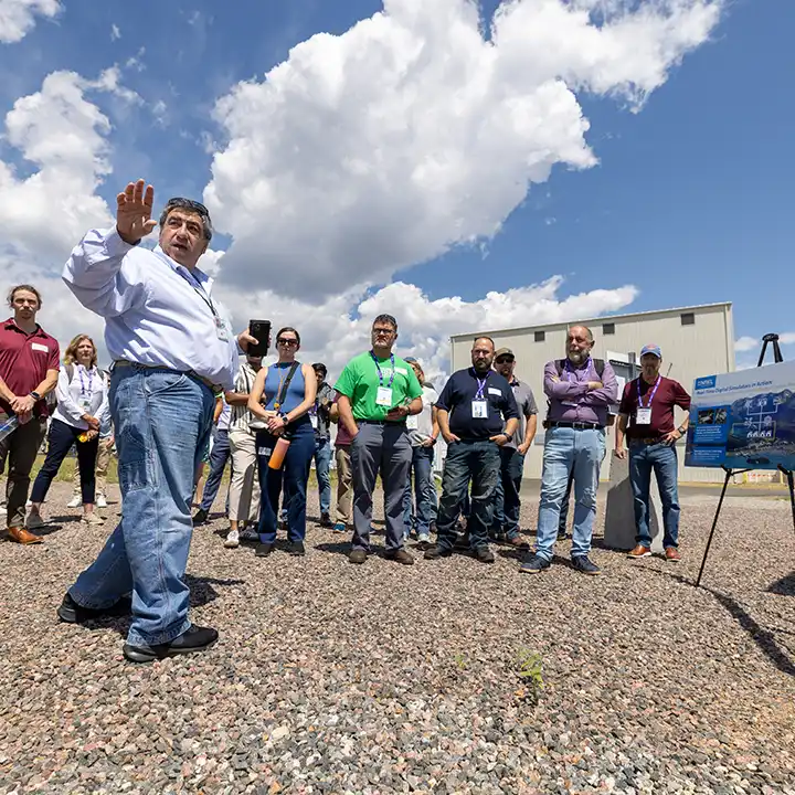 Group of people outside listening to presentation while one person points outward