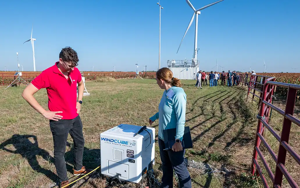 Two people stand in a field looking at a power box.